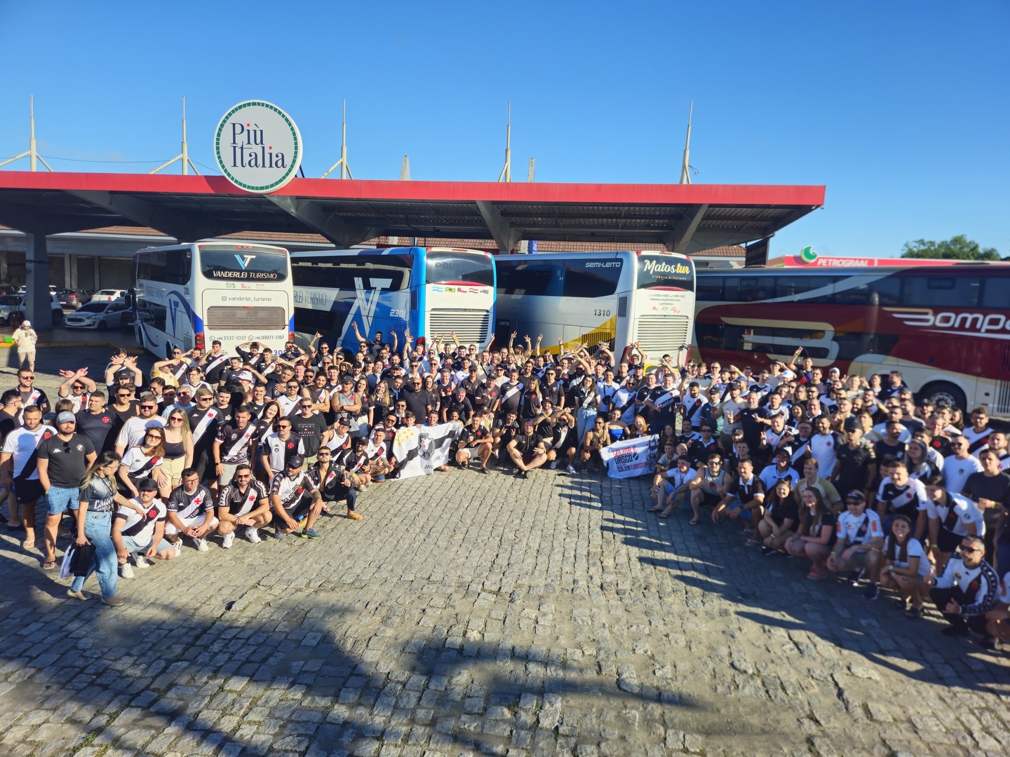 Grande grupo de passageiros reunido diante dos ônibus da caravana